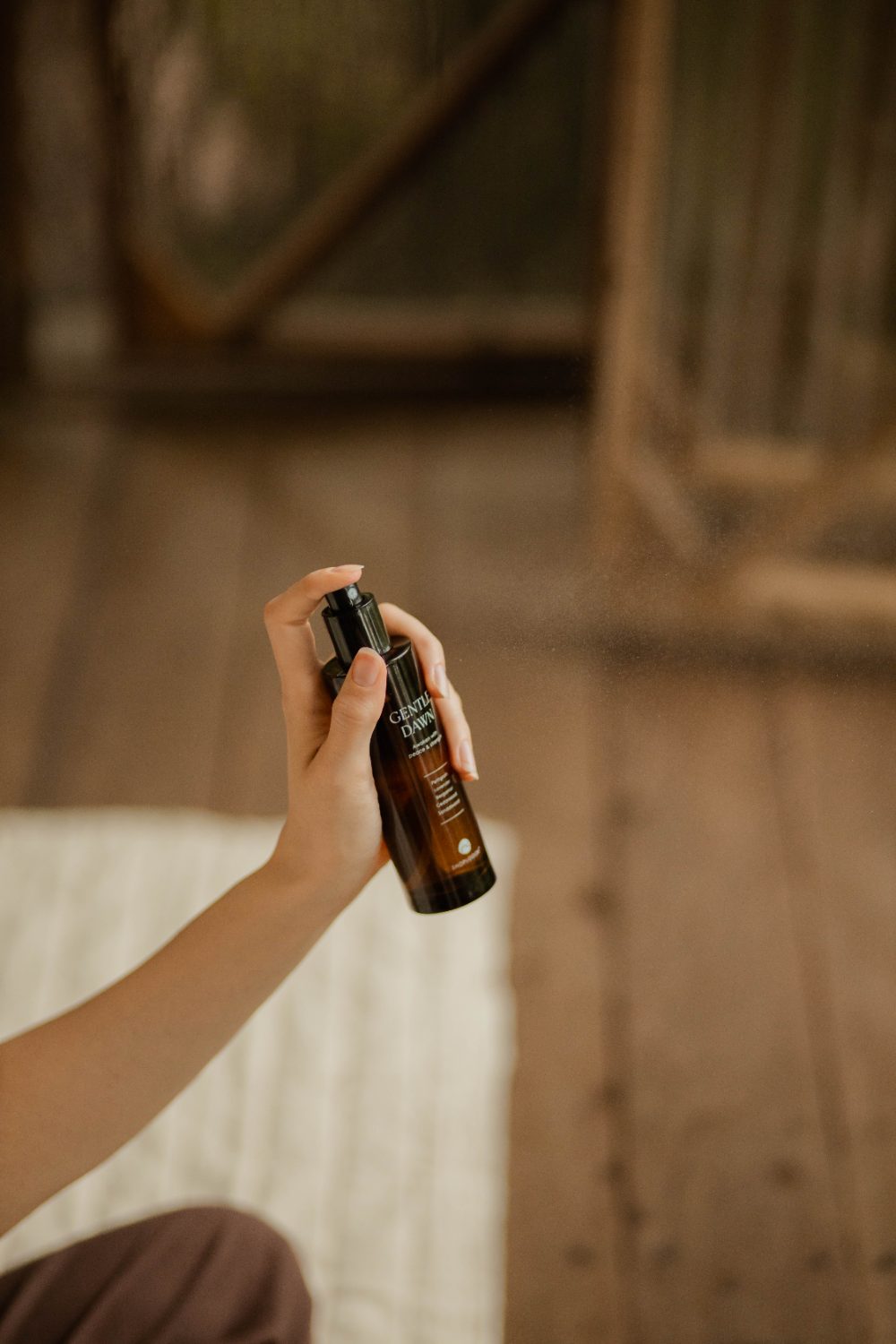 Hand misting the SHOPLOOOH Gentle Dawn room spray in a warm wooden interior