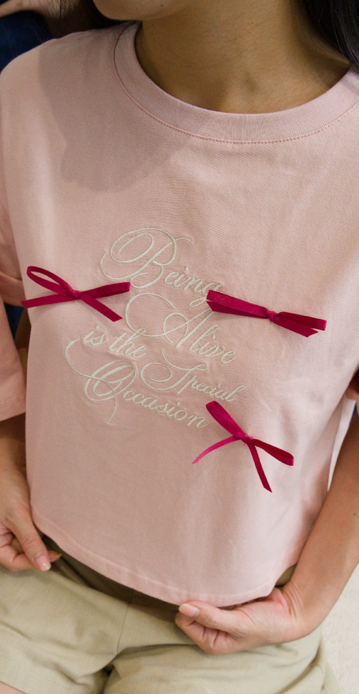 Close-up of hands resting on the hem of the pink Being Alive Is the Special Occasion Tee