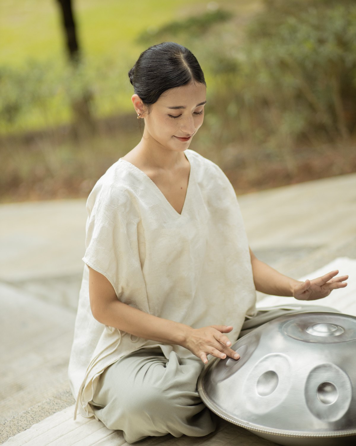 Playing a handpan in the SHOPLOOOH Re Collection natural white V-neck top and soft sage trousers